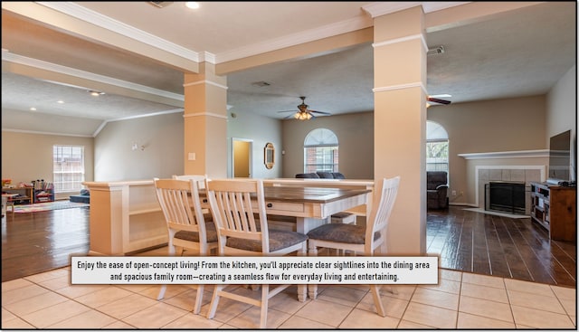 tiled dining space with decorative columns, ceiling fan, ornamental molding, visible vents, and a tiled fireplace