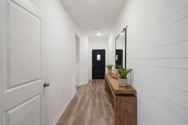 hallway with light wood finished floors, visible vents, and baseboards