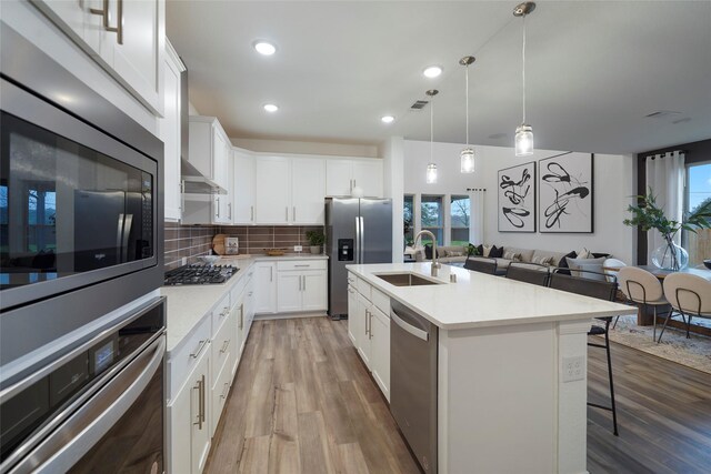kitchen with tasteful backsplash, light wood-type flooring, light countertops, appliances with stainless steel finishes, and a sink