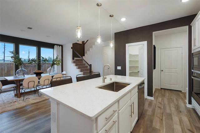 kitchen with pendant lighting, white cabinets, dishwasher, a sink, and wood finished floors