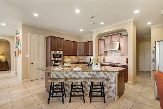 3203 Round Meadow Ln, Missouri City, TX 77459 - kitchen with light stone countertops, arched walkways, under cabinet range hood, stainless steel appliances, and a center island with sink