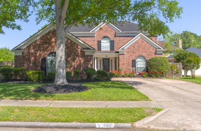traditional-style home featuring brick siding, a front yard, and driveway