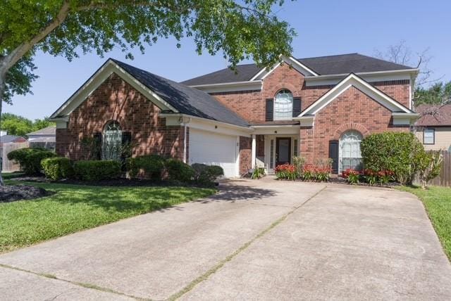 traditional-style home with brick siding, a front yard, an attached garage, and driveway