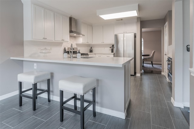 kitchen with wall chimney exhaust hood, stainless steel appliances, a peninsula, a sink, and white cabinets