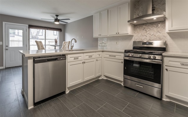 kitchen with stainless steel appliances, a sink, wall chimney exhaust hood, a peninsula, and decorative backsplash