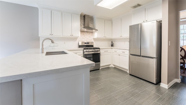 kitchen featuring appliances with stainless steel finishes, a sink, wall chimney range hood, a peninsula, and light countertops