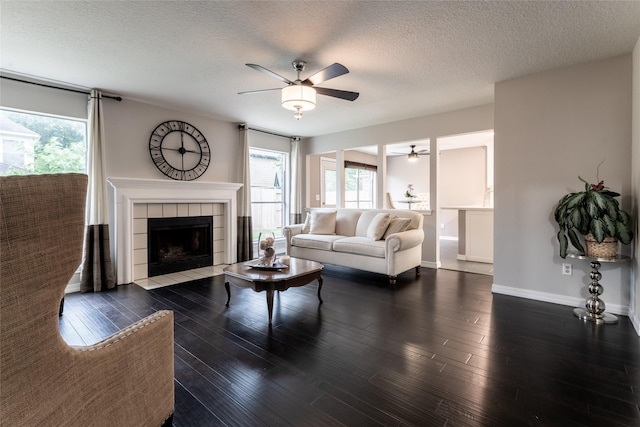 living area with a ceiling fan, healthy amount of natural light, wood finished floors, baseboards, and a textured ceiling