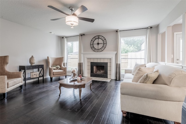 living area featuring dark wood-style floors, ceiling fan, a tiled fireplace, and baseboards