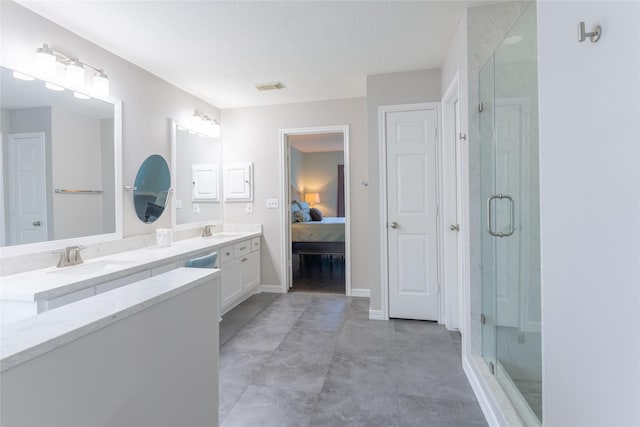 ensuite bathroom featuring a stall shower, double vanity, a textured ceiling, and baseboards