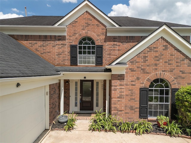 property entrance with brick siding, a shingled roof, and concrete driveway