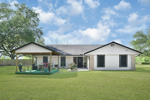 back of house featuring a shingled roof, brick siding, fence, and a lawn