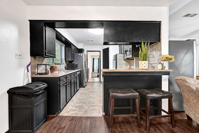 kitchen featuring visible vents, light countertops, a kitchen breakfast bar, dark cabinetry, and wood finished floors