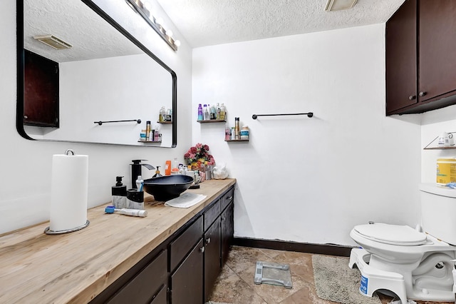 bathroom with toilet, baseboards, vanity, and a textured ceiling