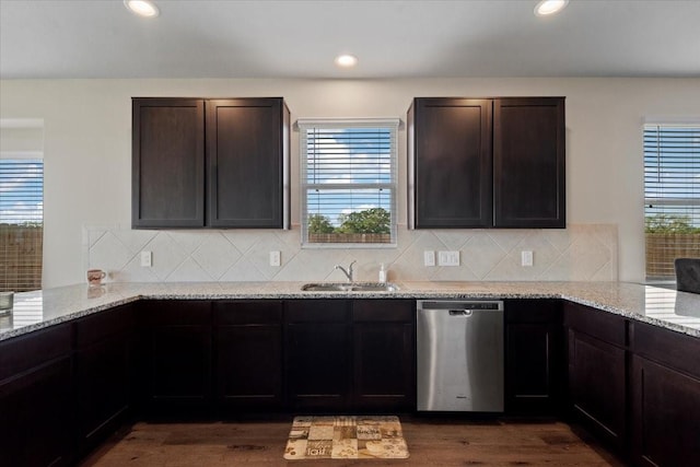 kitchen with light stone counters, backsplash, dark wood finished floors, stainless steel dishwasher, and a sink
