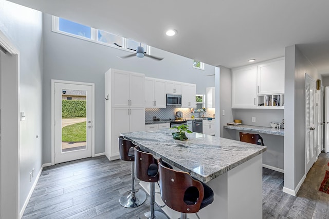 kitchen featuring appliances with stainless steel finishes, a kitchen breakfast bar, white cabinetry, wood finished floors, and a wealth of natural light