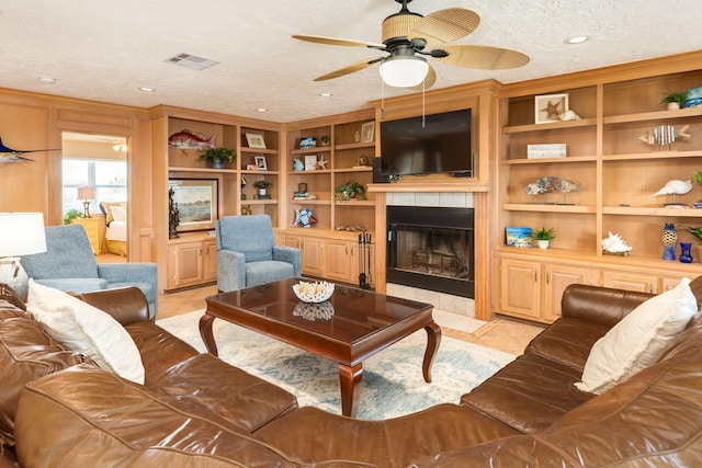 living room featuring built in features, a textured ceiling, visible vents, ceiling fan, and a tile fireplace