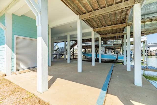 view of patio with a water view, a carport, boat lift, and a dock