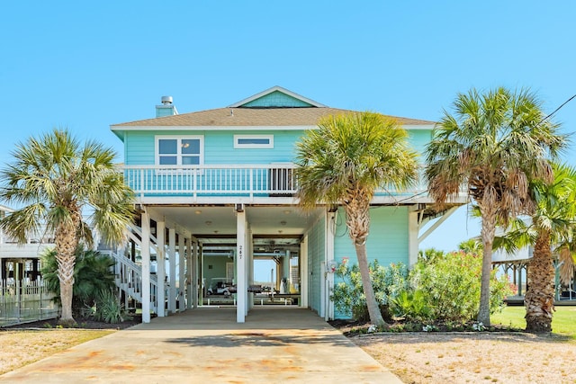 coastal inspired home with a carport, covered porch, a chimney, stairway, and driveway