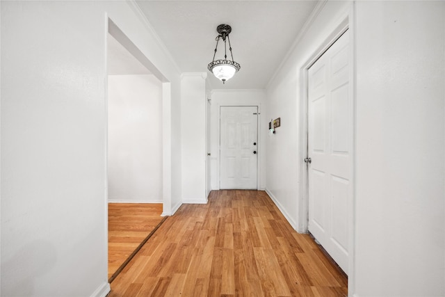 hall featuring ornamental molding, baseboards, and light wood-style floors