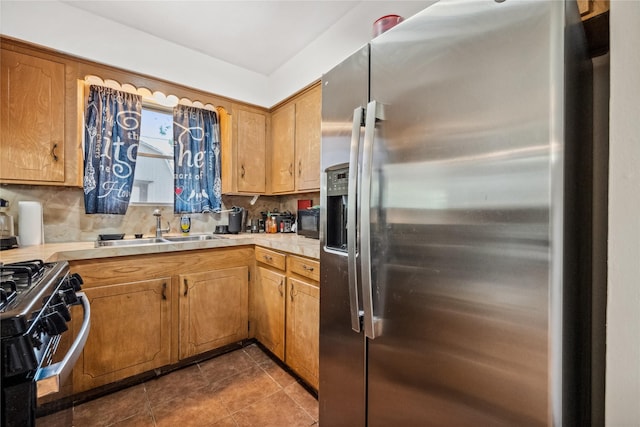 kitchen featuring stainless steel refrigerator with ice dispenser, a sink, light countertops, range with gas stovetop, and dark tile patterned floors
