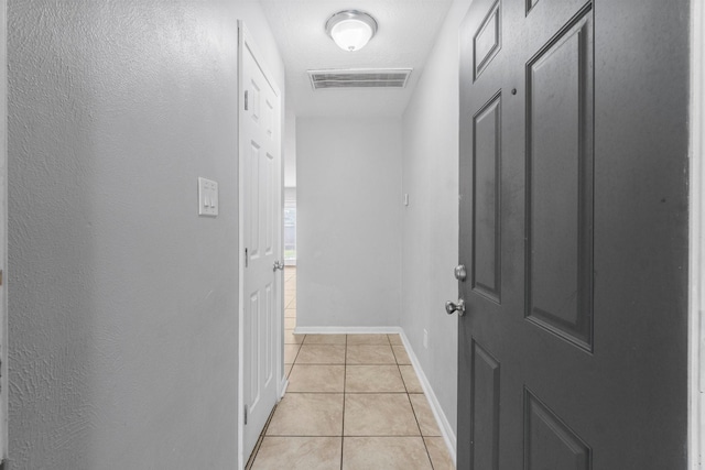 hall featuring baseboards, visible vents, and light tile patterned floors