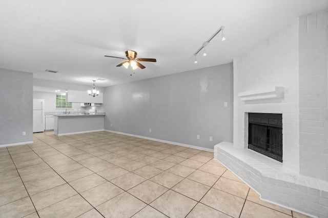 unfurnished living room featuring a sink, a brick fireplace, rail lighting, ceiling fan with notable chandelier, and light tile patterned floors