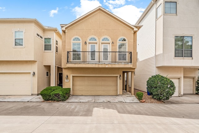 view of property with an attached garage, concrete driveway, a balcony, and stucco siding