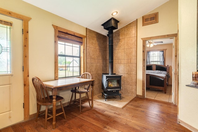 dining area featuring lofted ceiling, wood finished floors, a wood stove, visible vents, and baseboards