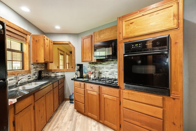 kitchen featuring light wood finished floors, dark countertops, a sink, decorative backsplash, and black appliances
