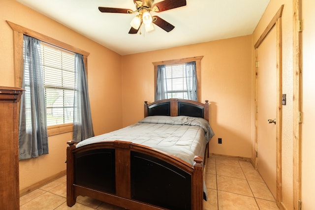 bedroom featuring a ceiling fan, baseboards, light tile patterned flooring, and multiple windows