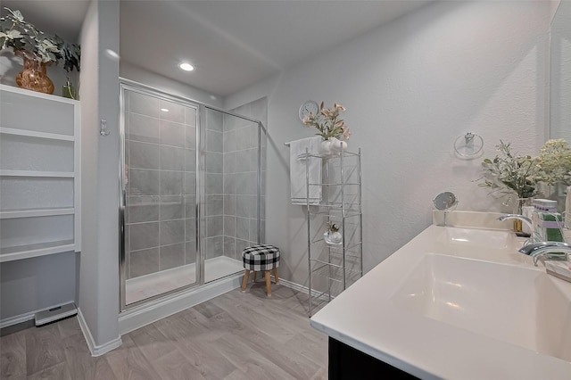 full bathroom featuring baseboards, double vanity, a shower stall, a sink, and wood finished floors