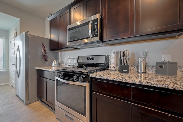 kitchen featuring dark brown cabinets, light wood-type flooring, appliances with stainless steel finishes, and light stone counters
