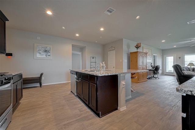 kitchen featuring visible vents, appliances with stainless steel finishes, a sink, open floor plan, and a center island with sink