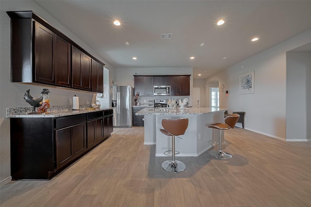 kitchen featuring visible vents, a breakfast bar, dark brown cabinetry, stainless steel appliances, and light wood-style flooring