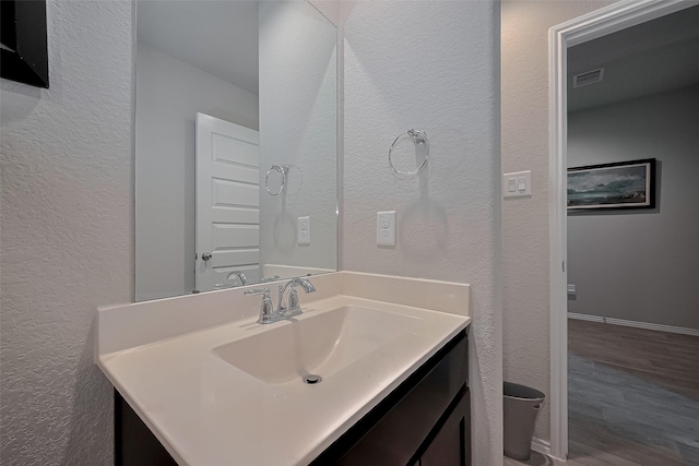 bathroom with visible vents, a textured wall, vanity, and wood finished floors