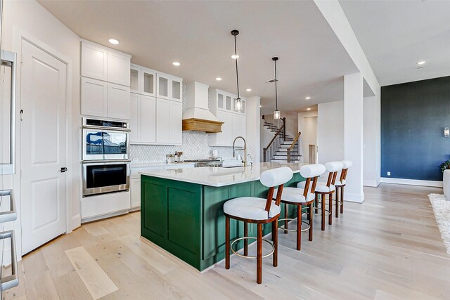 7606 Redwoods Forest Dr, Katy, TX 77493 - kitchen with white cabinets, a sink, light wood finished floors, custom range hood, and stainless steel double oven