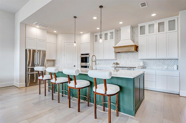 7606 Redwoods Forest Dr, Katy, TX 77493 - kitchen with custom exhaust hood, appliances with stainless steel finishes, light wood finished floors, and visible vents