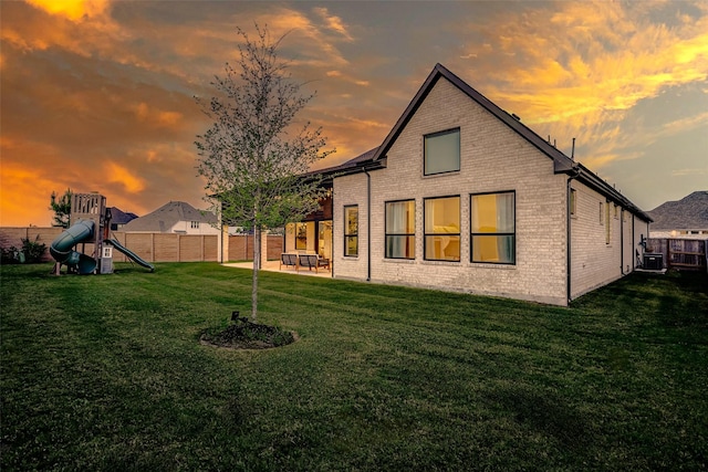 7606 Redwoods Forest Dr, Katy, TX 77493 - back of property at dusk with a fenced backyard, a lawn, a patio, a playground, and brick siding