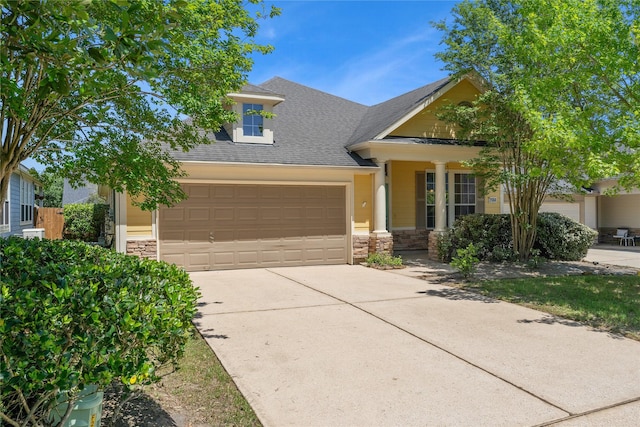 view of front facade with a shingled roof, driveway, stone siding, and an attached garage