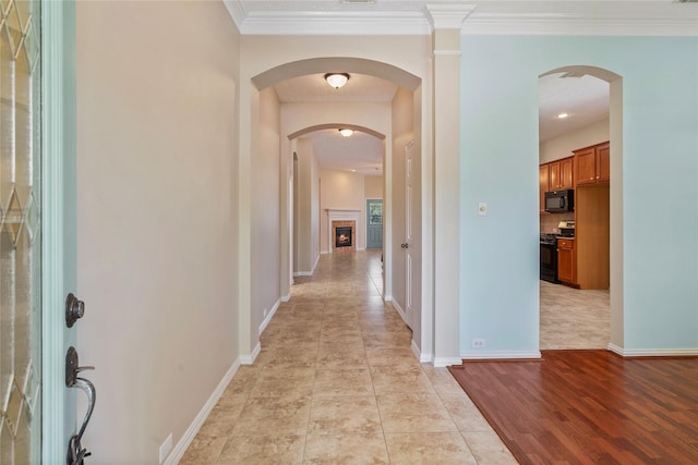 hall featuring arched walkways, baseboards, and crown molding