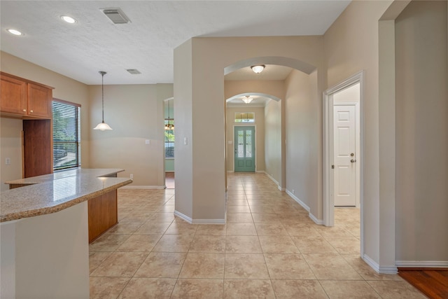 interior space featuring light tile patterned floors, light stone countertops, arched walkways, visible vents, and brown cabinets