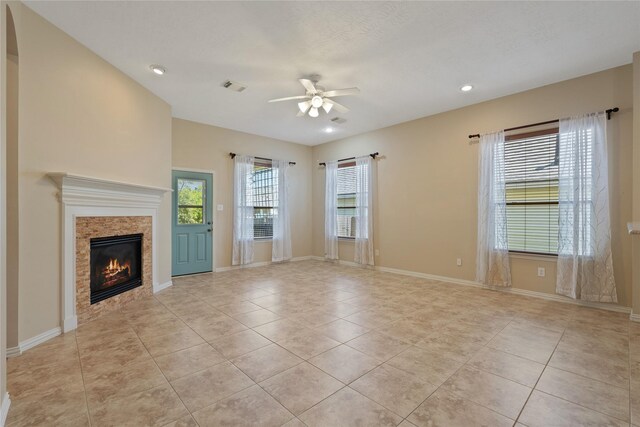 unfurnished living room featuring ceiling fan, a glass covered fireplace, visible vents, light tile patterned flooring, and baseboards