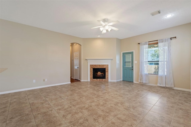 unfurnished living room featuring a lit fireplace, baseboards, visible vents, ceiling fan, and arched walkways