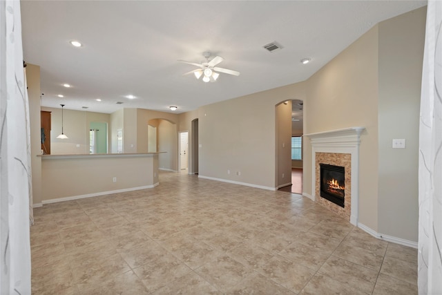 unfurnished living room featuring arched walkways, a tiled fireplace, baseboards, and a ceiling fan