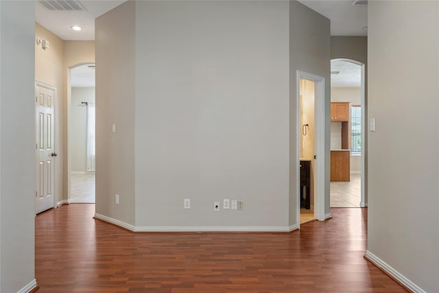 unfurnished room featuring arched walkways, dark wood-style flooring, baseboards, and visible vents