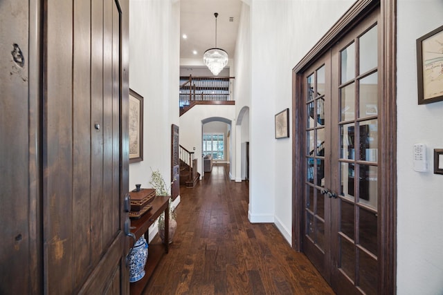 corridor featuring dark wood-style flooring, baseboards, stairway, french doors, and arched walkways