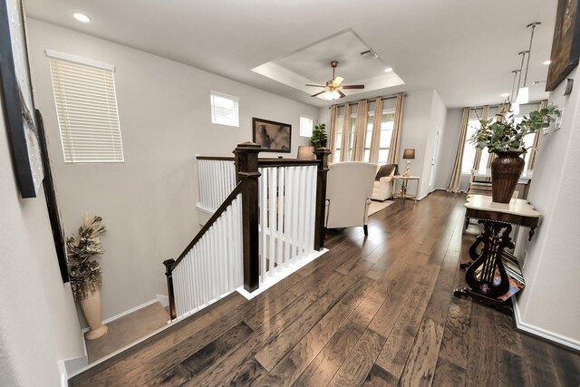 hallway with wood-type flooring, baseboards, recessed lighting, a tray ceiling, and an upstairs landing