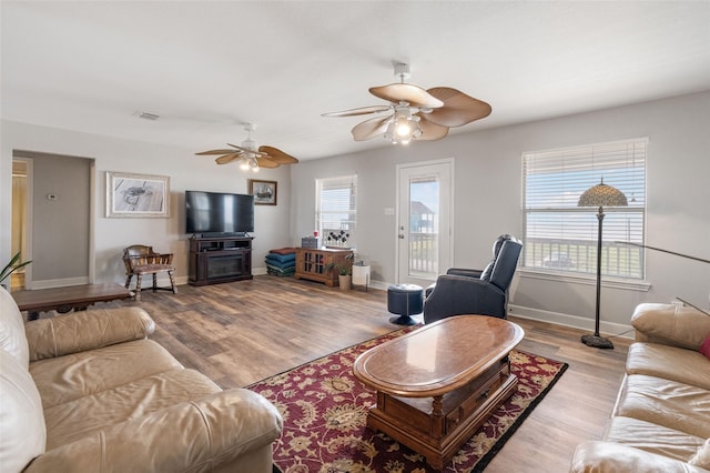 living area featuring visible vents, baseboards, a ceiling fan, and wood finished floors