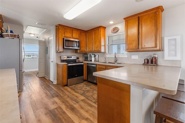 kitchen with light wood-type flooring, a peninsula, light countertops, stainless steel appliances, and a sink