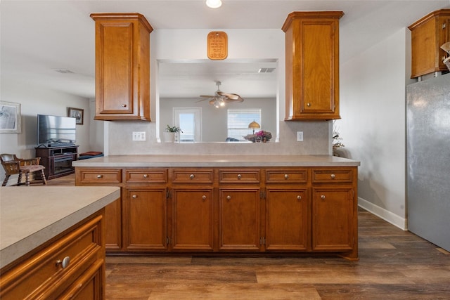 kitchen with brown cabinetry, light countertops, freestanding refrigerator, and a ceiling fan